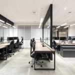 Ergonomiczna przestrzeń biurowa z nowoczesnymi stanowiskami pracy, drewnianymi biurkami i czarnymi krzesłami.