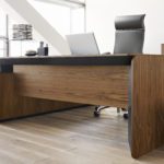 Projekt ergonomicznej przestrzeni biurowej: drewniane biurko, czarny fotel, jasna podłoga, dużo światła.