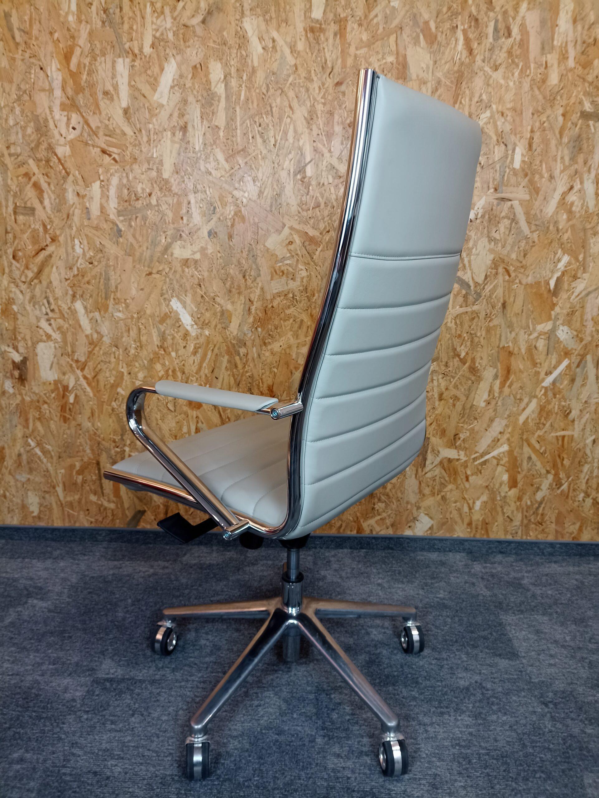 Nowoczesne ergonomiczne krzesło biurowe w jasnoszarym kolorze z chromowanymi elementami na tle płyty OSB.