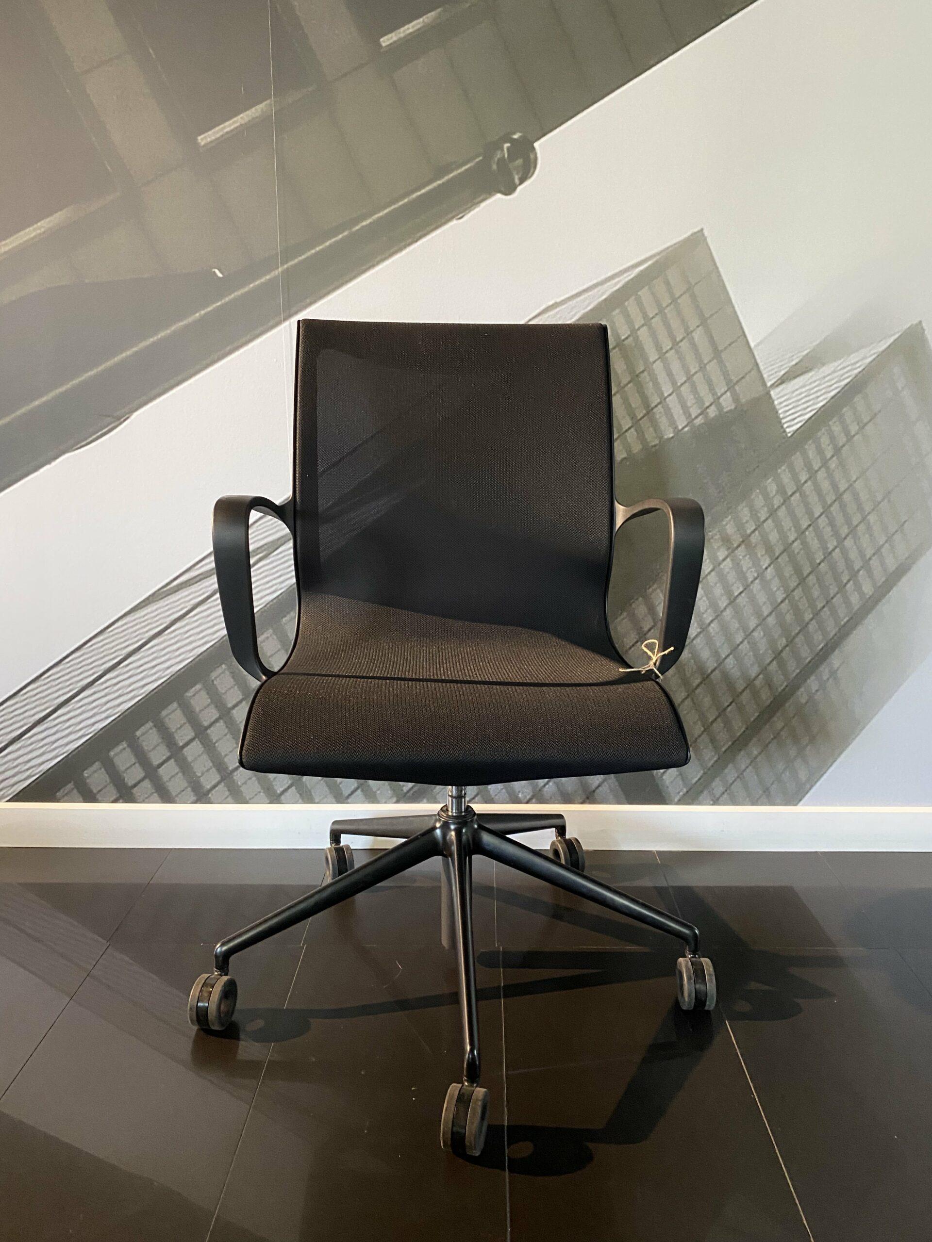 Ergonomiczne czarne krzesło biurowe na tle szarej grafiki nowoczesnych budynków.