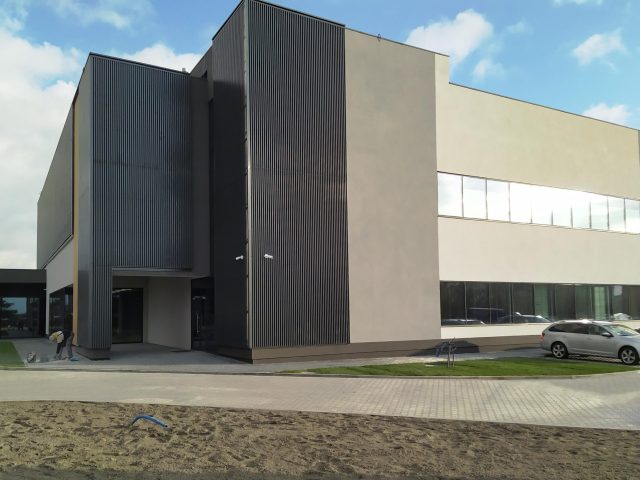 Kompleksowa realizacja nowoczesnego biurowca z ciemną fasadą i jasnymi panelami, błękitne niebo.