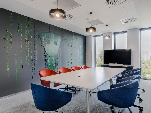 Ergonomiczna sala konferencyjna z nowoczesnymi meblami, ekranem multimedialnym oraz charakterystyczną grafiką na ścianie.
