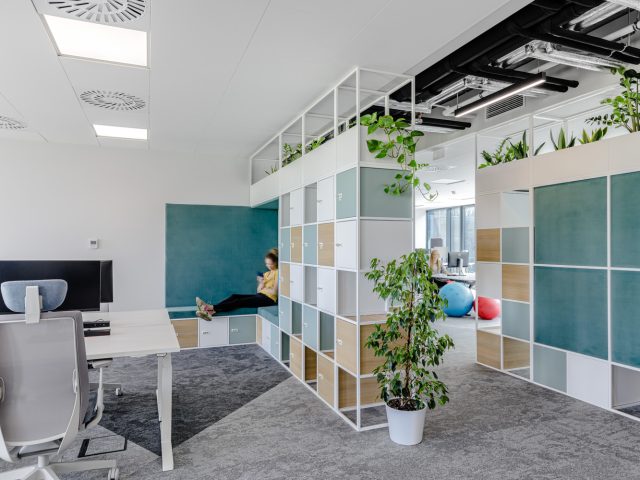 Aranżacja biura otwartej przestrzeni z ergonomicznymi stanowiskami, zielenią i komfortowymi strefami relaksu, turkusowe akcenty.
