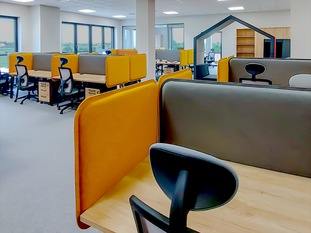 Ergonomiczne stanowiska pracy w biurze open space z żółto-szarymi panelami akustycznymi i meblami biurowymi.