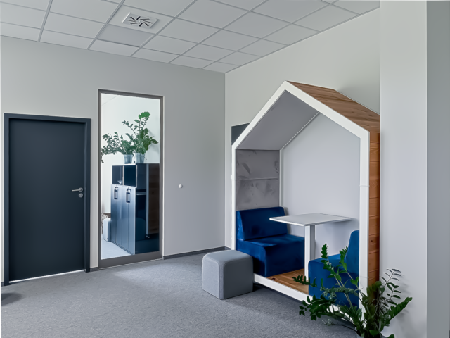Ergonomiczna przestrzeń biurowa z domkową budką do pracy cichej i niebieskimi siedziskami.