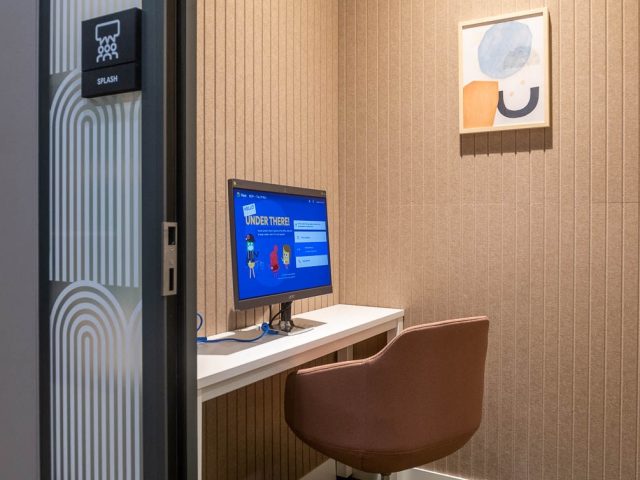 Nowoczesne, ergonomiczne stanowisko pracy z wygodnym fotelem, komputerem i beżowymi panelami akustycznymi.