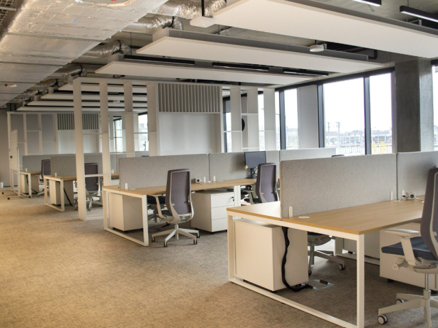 Nowocześnie zaprojektowana otwarta przestrzeń biurowa z ergonomicznymi stanowiskami pracy, jasnymi meblami i panelami akustycznymi.
