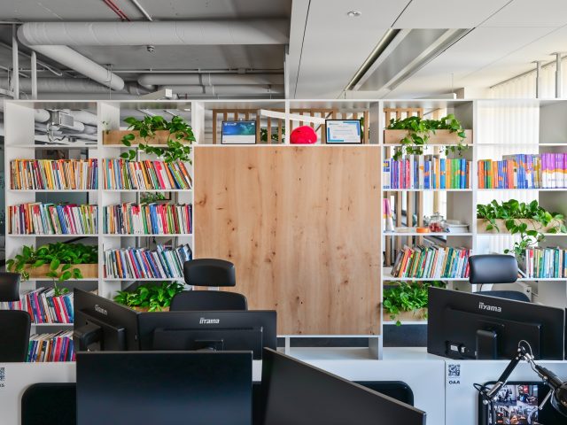 Nowoczesna, otwarta przestrzeń biurowa z białymi regałami, roślinami i ergonomicznymi stanowiskami pracy.