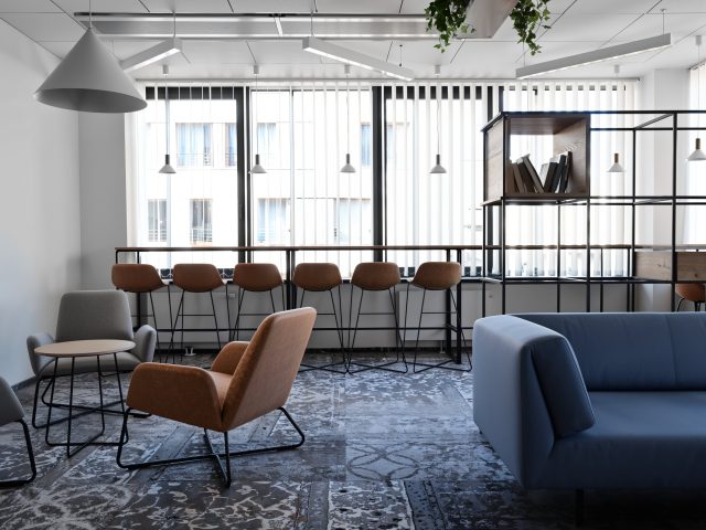 Ergonomiczna strefa współpracy biurowej LOGAN: niebieska sofa, brązowe fotele i wysoki blat.
