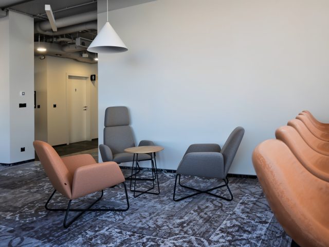 Projekt ergonomicznej strefy lounge w biurze, z komfortowymi fotelami w odcieniach szarości i brązu