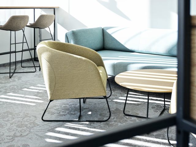 Projekt aranżacji strefy relaksu w biurze, jasnoniebieska sofa, beżowy fotel, nowoczesny stolik kawowy.